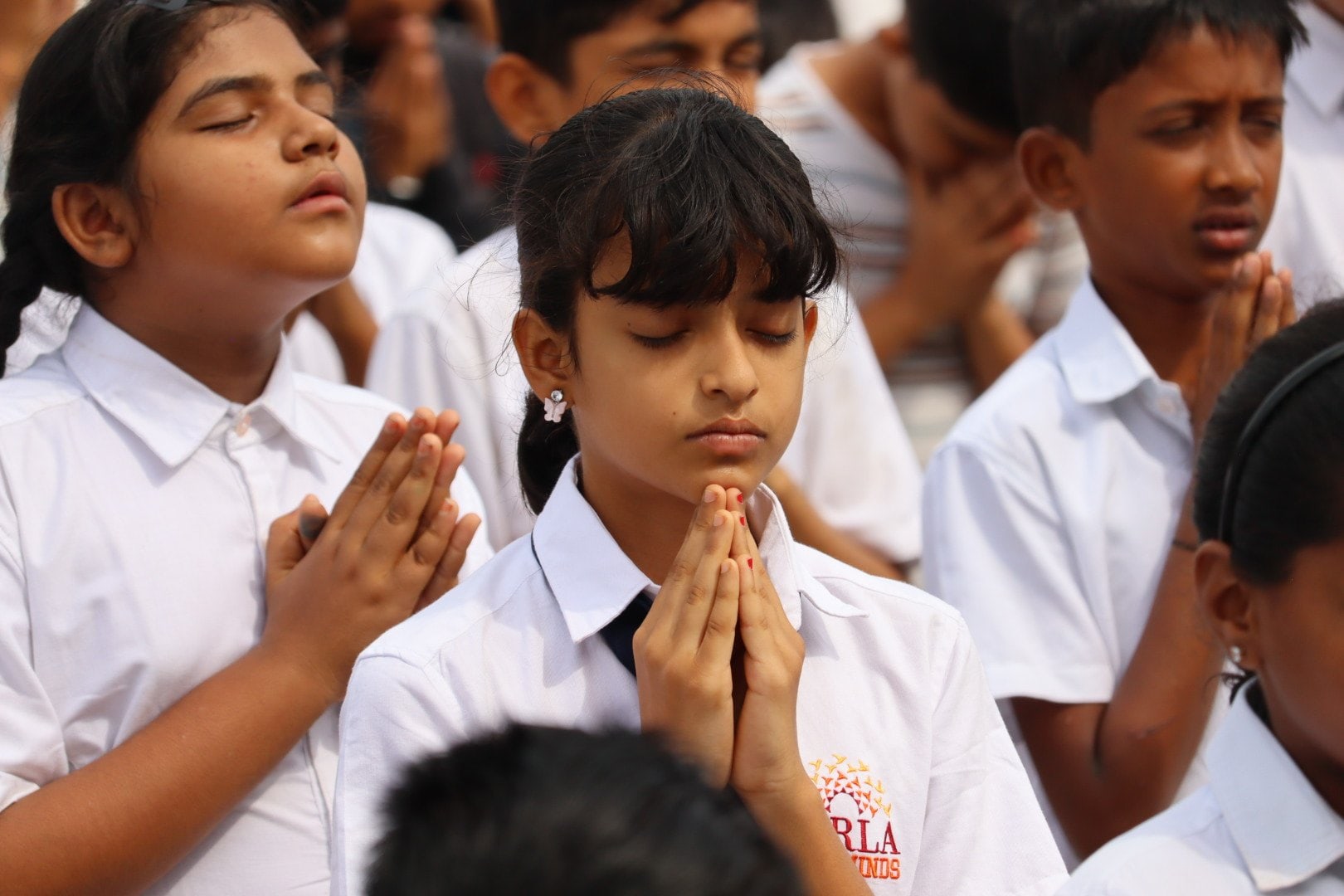 Students of SHLOKA - A Birla School standing with hands folded, eyes closed, during the morning prayer at assembly