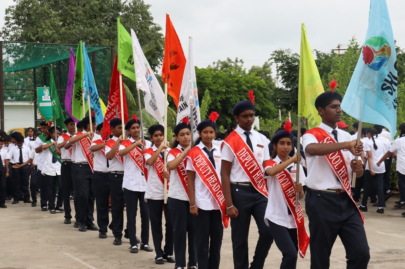 Students marching with house flags along a paved path on the school campus